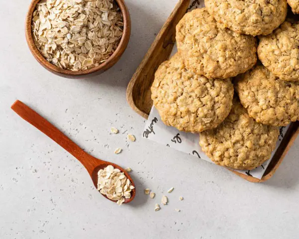 Biscotti di avena dorati e croccanti, con fiocchi d'avena in una ciotola e un cucchiaio.