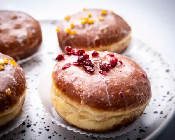 Paczki ricchi e golosi, con glassa lucida e decorazioni di frutta secca. Un invito a provare il paczki przepis perfetto.