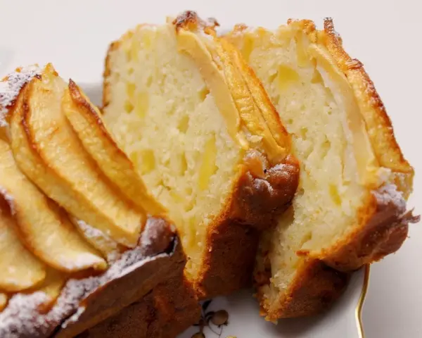 Fette di plumcake ricotta e mele, con mele a vista sulla superficie e spolverata di zucchero a velo.