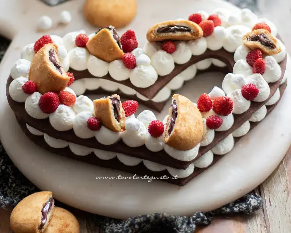 Cuore di pasta biscotto al cacao per cream tart, decorato con panna, fragoline e biscotti ripieni.