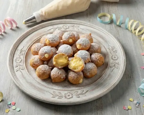 Castagnole ripiene di crema, spolverate di zucchero a velo, pronte per Carnevale. Un'idea golosa con yogurt greco per un tocco fresco.