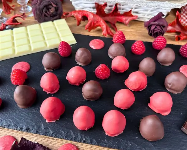 Cioccolatini al lampone, alcuni ricoperti di cioccolato fondente, altri di rosa, con lamponi freschi e tavoletta di cioccolato bianco.