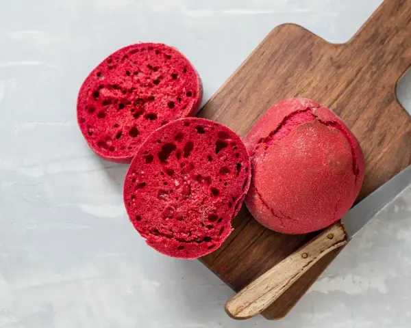 Pane alla barbabietola, un panino rosso vibrante tagliato a metà su un tagliere di legno, pronto per essere gustato.