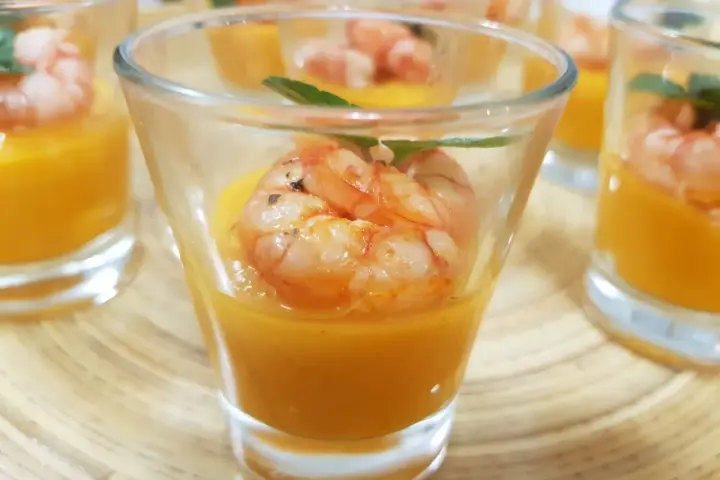 Deliziosi gamberi aperitivo in bicchierini con crema arancione e foglioline verdi.