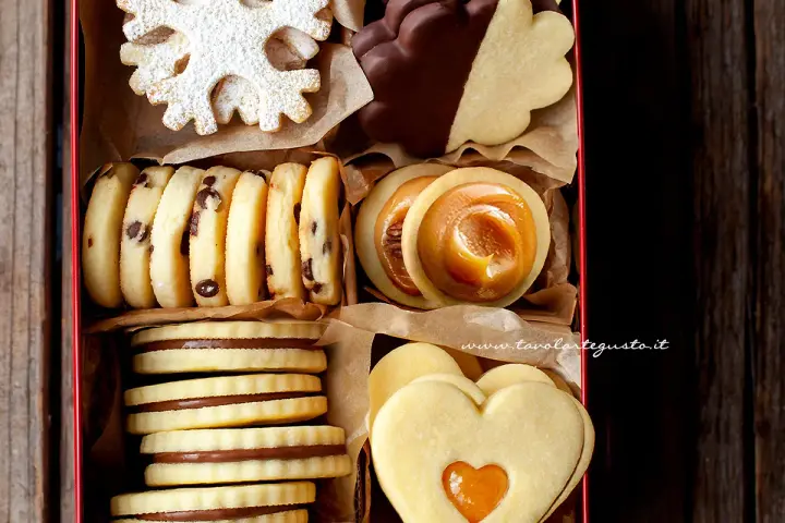 Scatola piena di deliziosi ciasteczka maślane: a fiocco di neve, al cioccolato, con ripieno di caramello e a forma di cuore.