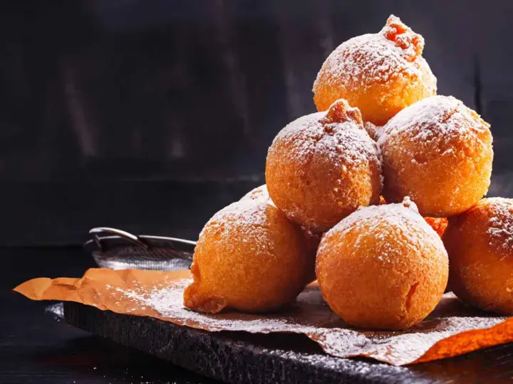 Pile di frittelle di mele e uvetta con lievito di birra, spolverate di zucchero a velo, su carta da forno.