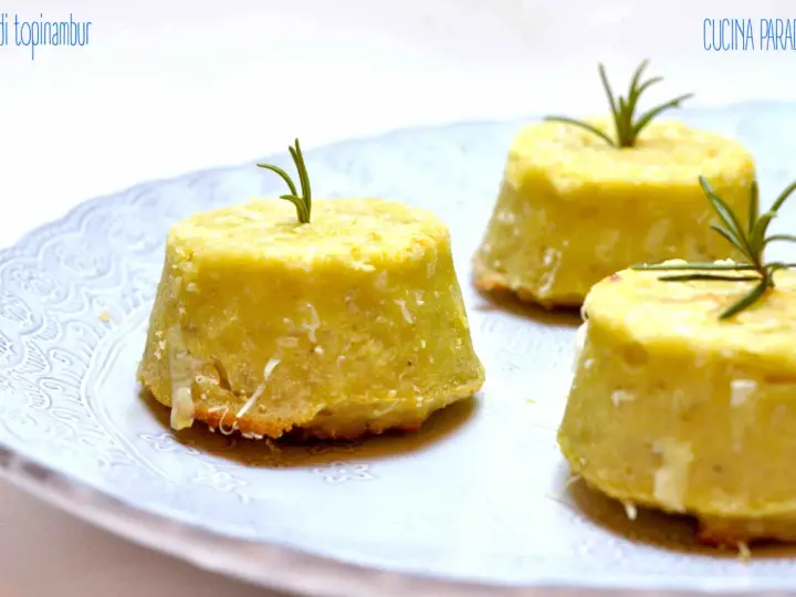 Flan di topinambur senza patate, dorati e profumati, guarniti con rosmarino fresco su un piatto bianco decorato.