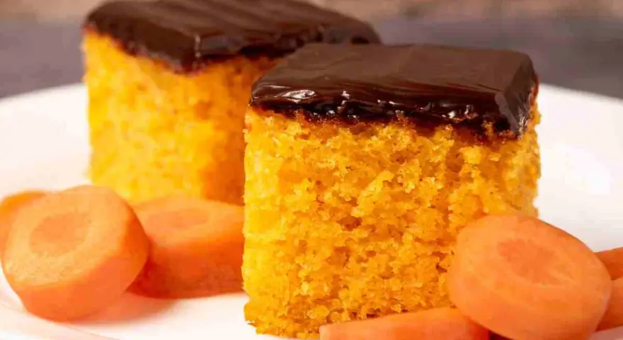 Due fette di ciasto marchewkowe, soffice e arancione, ricoperte di glassa al cioccolato fondente, con fettine di carota fresca intorno.
