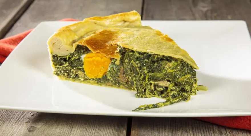 Una fetta di torta di bietole e ricotta senza sfoglia, con un uovo intero al centro, su un piatto bianco.