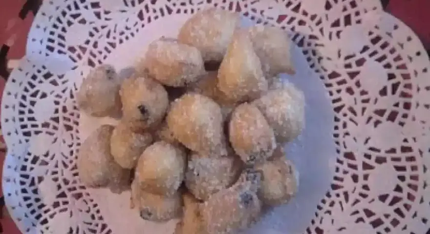 Un mucchietto di castagnole montersino, dolcetti dorati e zuccherati, adagiati su un centrino di pizzo bianco.