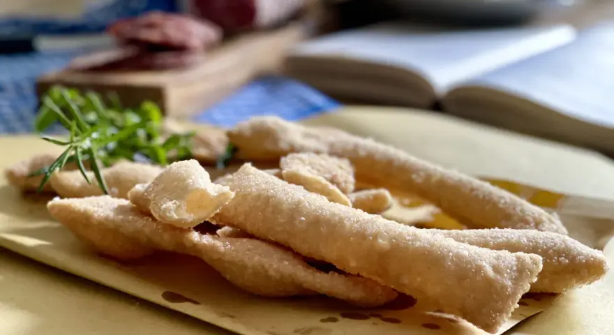 Sgabei fritti dorati e croccanti, profumati con rosmarino fresco, pronti per essere gustati con salumi e formaggio.