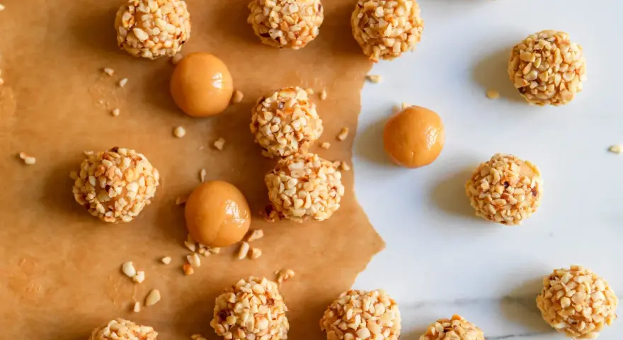Piccoli bomboloni caramelle ricoperti di noccioline tritate, alcuni con un ripieno di caramello visibile.