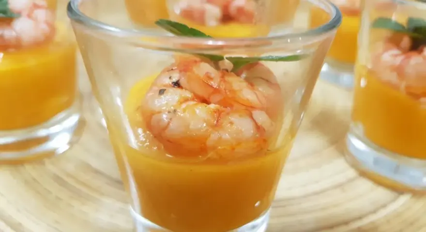 Deliziosi gamberi aperitivo in bicchierini con crema arancione e foglioline verdi.