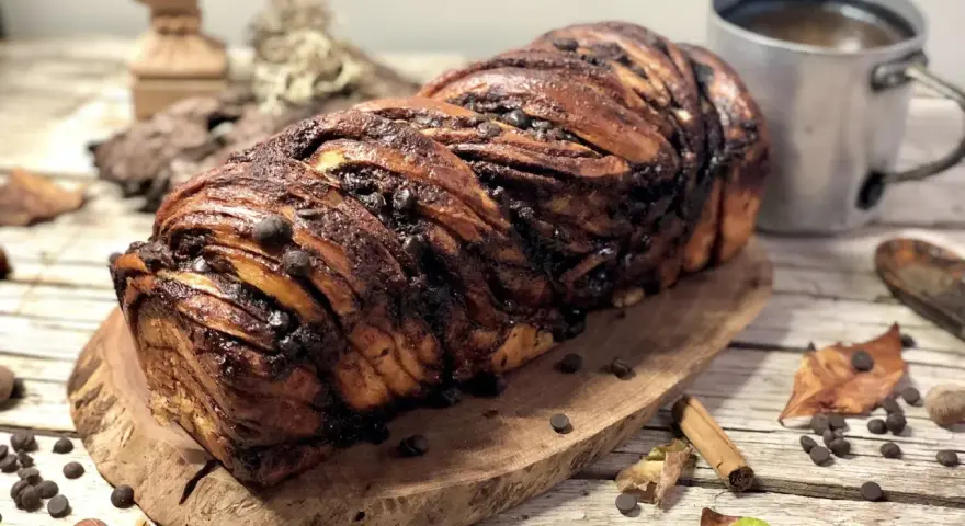 Babka ponczowa, intrecciata e ricca di gocce di cioccolato, pronta per essere gustata con una tazza di caffè.