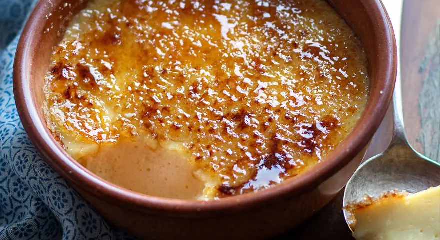 Un delizioso krem kataloński con crosta caramellata dorata, servito in una ciotola di terracotta.