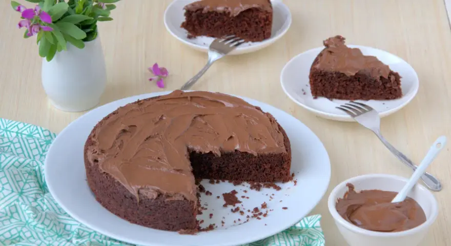 Deliziosa torta al cioccolato senza glutine con fecola di patate, ricoperta di glassa al cioccolato, servita su piatti bianchi con forchette.