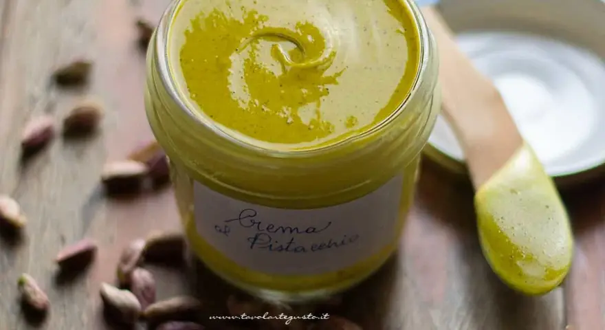 Un vasetto di cremosa crema di pistacchio, con pistacchi sparsi intorno. Perfetta per dolci e colazioni.