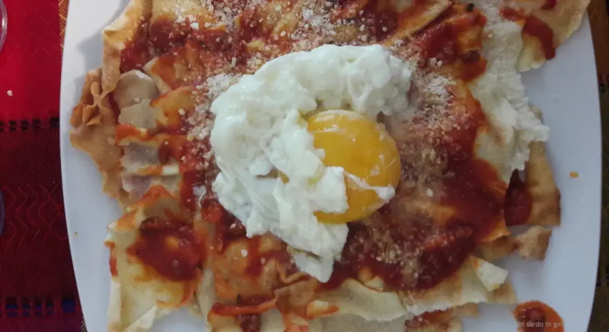 Spianata sarda come farcirla: croccante base con sugo rosso, formaggio grattugiato e un uovo in camicia.