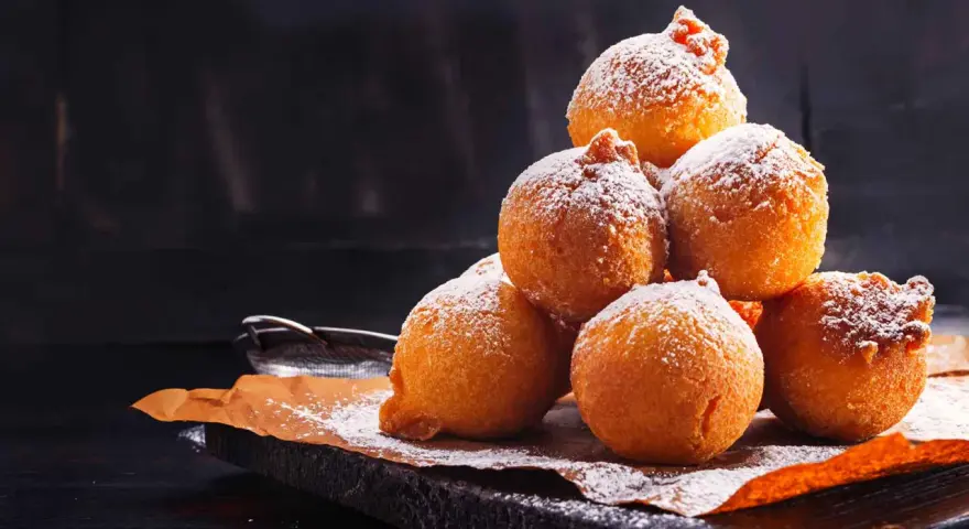 Pile di frittelle di mele e uvetta con lievito di birra, spolverate di zucchero a velo, su carta da forno.