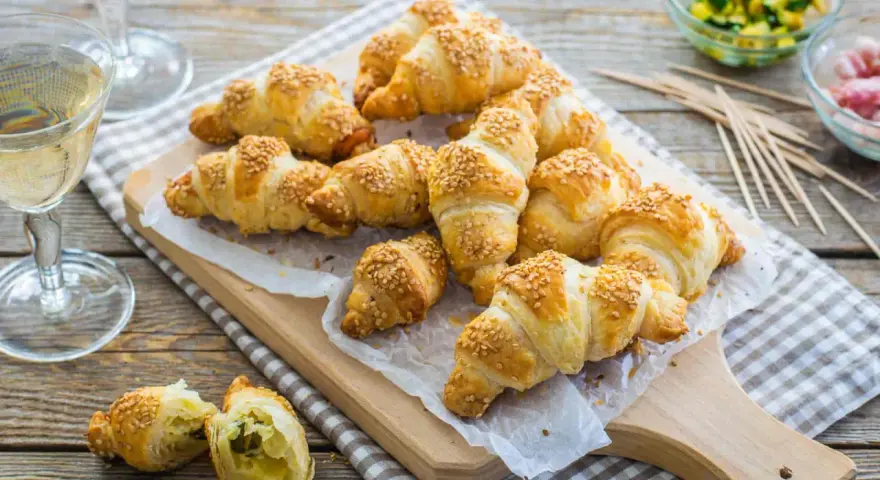 Croissant dorati con ripieno di pasta sfoglia e semi di sesamo, pronti per essere gustati con un bicchiere di vino.