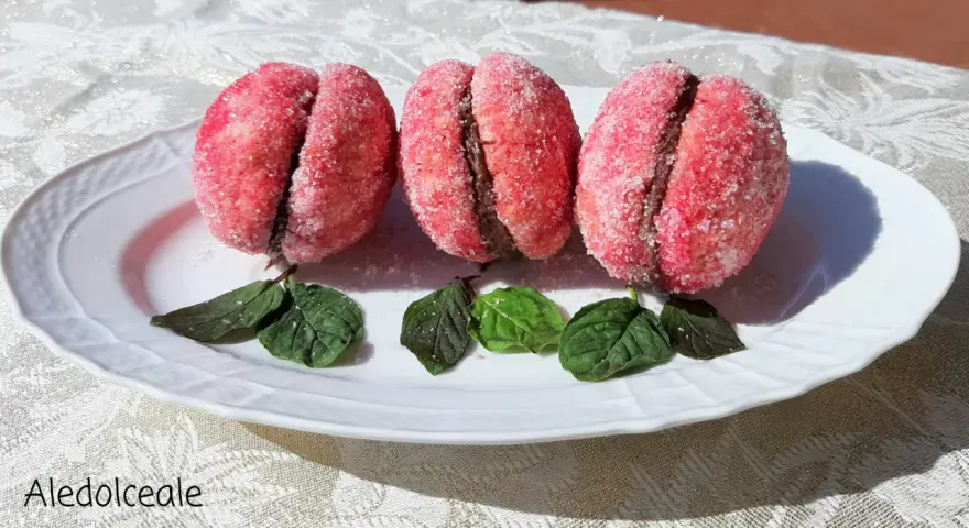 Tre dolci pesche abruzzesi ricoperte di zucchero, con un ripieno scuro, adagiate su un piatto bianco con foglie verdi.