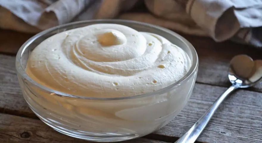 Una ciotola di soffice crema al mascarpone senza lattosio, pronta per essere gustata. Un cucchiaino argentato attende accanto.