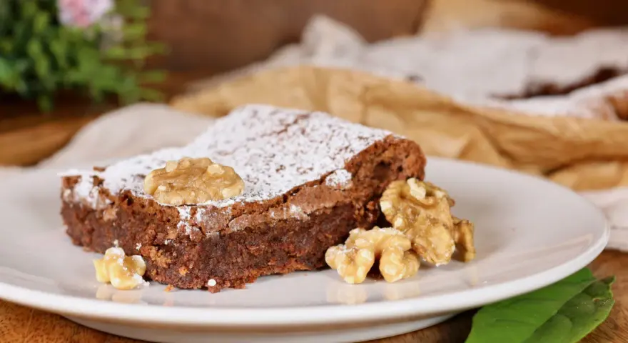 Una fetta di torta noci e cioccolato senza farina, cosparsa di zucchero a velo e decorata con noci intere.