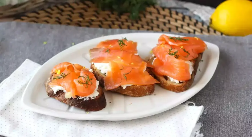 Tre bruschette con salmone affumicato, formaggio cremoso e aneto, guarnite con scorza di limone.