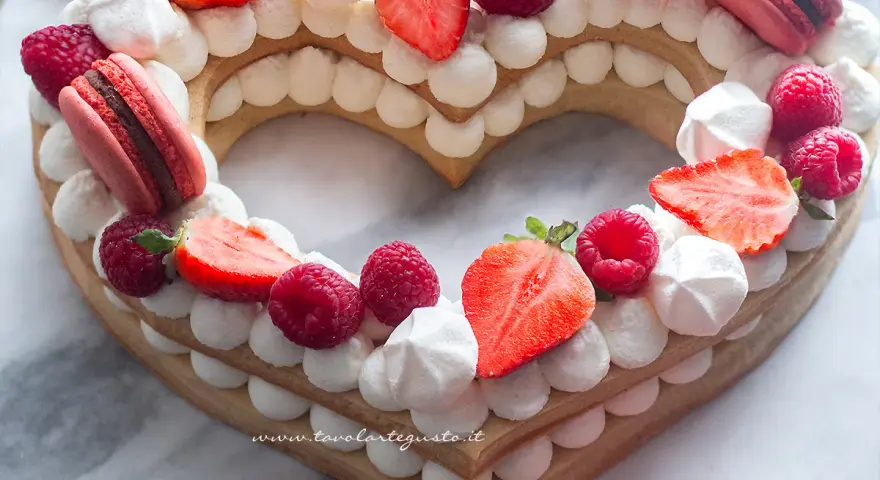 Cream tart numero 1 a forma di cuore, decorata con panna, fragole, lamponi e macarons.