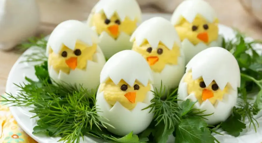 Uova sode ripiene a forma di pulcino, un'idea divertente per le jajka faszerowane pasquali, adagiate su un letto di erbe aromatiche.