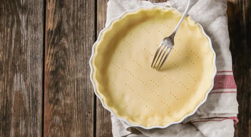 Pasta frolla salata con olio e parmigiano pronta per essere infornata. Una forchetta è appoggiata sulla base bucherellata.