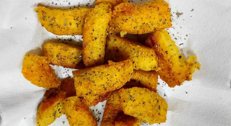 Croccanti bastoncini di polenta taragna fritta, dorati e conditi con erbe aromatiche, adagiati su carta bianca.