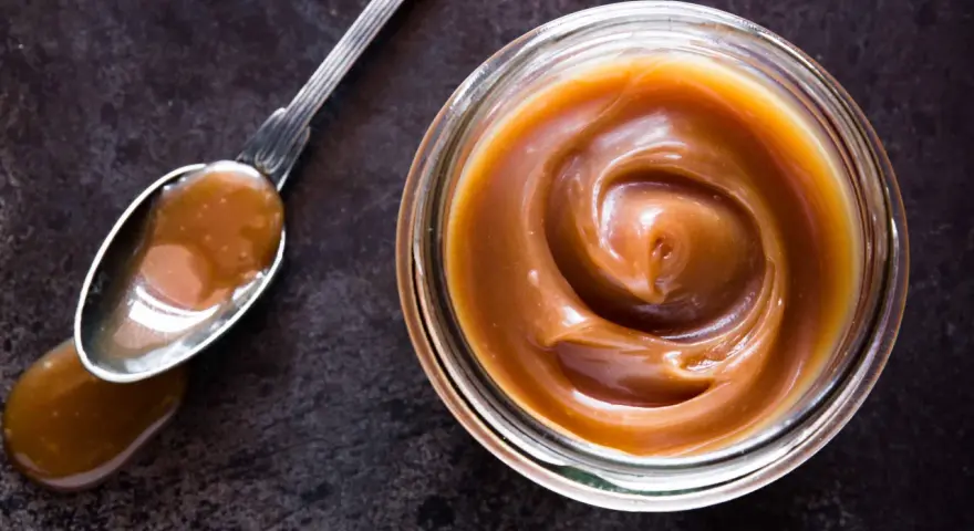 Un cucchiaio pieno di crema pasticcera al caramello salato, accanto a un barattolo dello stesso delizioso composto.