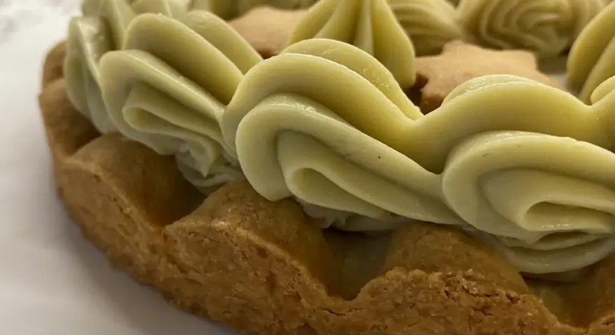 Torta con bordi croccanti e un abbondante strato di ganache pistacchio, decorata con biscotti a forma di stella.