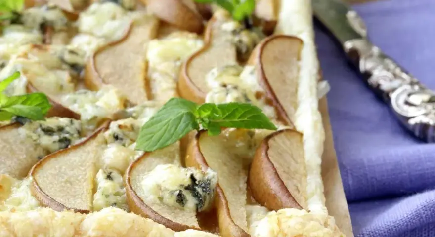 Deliziosa pizza zola e pere su pasta sfoglia croccante, guarnita con foglie di menta fresca. Un connubio di sapori unico.