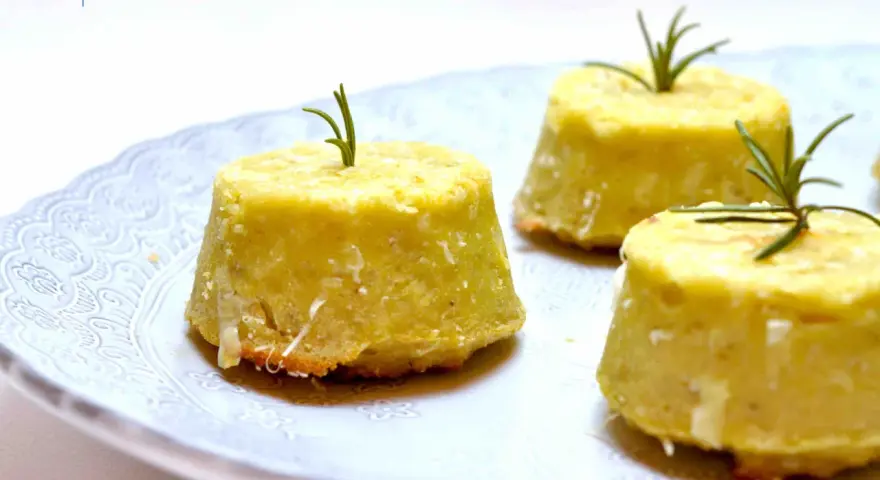 Flan di topinambur senza patate, dorati e profumati, guarniti con rosmarino fresco su un piatto bianco decorato.