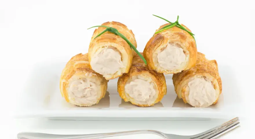 Cannoli salati ripieni di tonno, guarniti con erba cipollina, su un piatto bianco con forchetta.