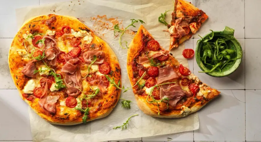 Pizza con mascarpone, pomodorini, prosciutto crudo e rucola, su carta forno.