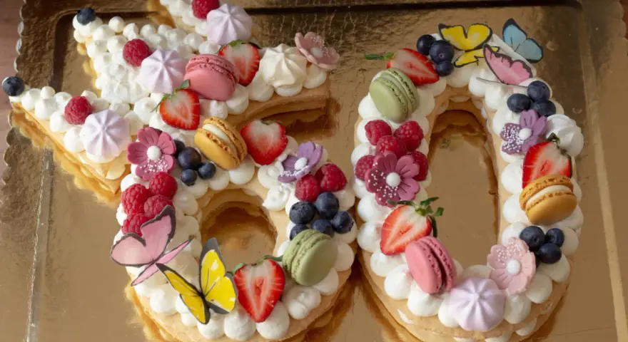 Una torta numero 60 decorata con panna, frutta fresca, macarons e farfalle. Una deliziosa ricetta torta numero per festeggiare.