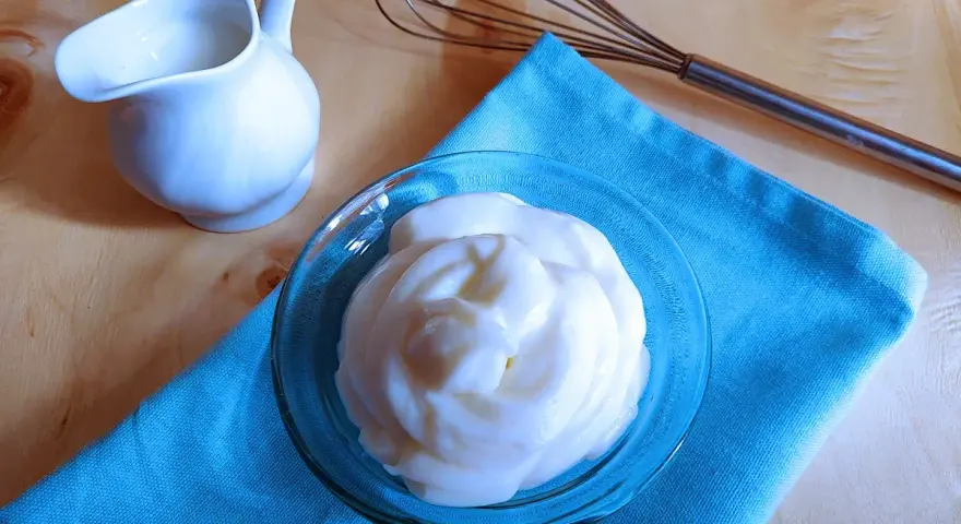 Crema soffice e vellutata, una delizia preparata con yogurt greco. Accanto, una piccola brocca e una frusta, pronti per creare altre bontà.