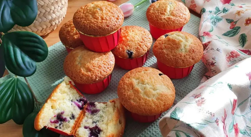 Morbidi muffin ai mirtilli, uno tagliato a metà rivela il suo interno succoso. Perfetti per una colazione o merenda golosa.