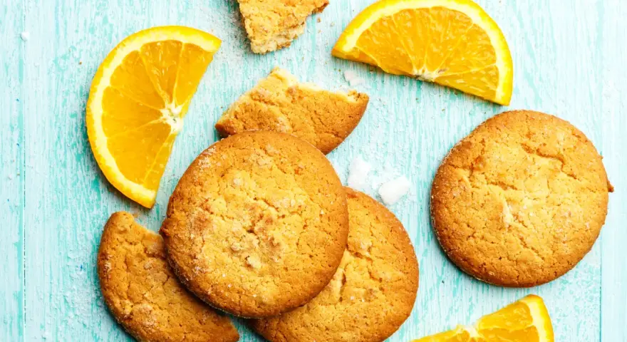 Biscotti all'arancia ricetta della nonna: dolci profumati e dorati, con spicchi d'arancia fresca su un tavolo di legno azzurro.