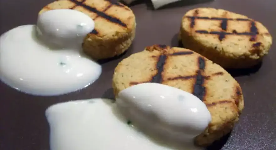 Deliziosi medaglioni di ceci grigliati, serviti con una salsa bianca cremosa e guarniti con erbe aromatiche.