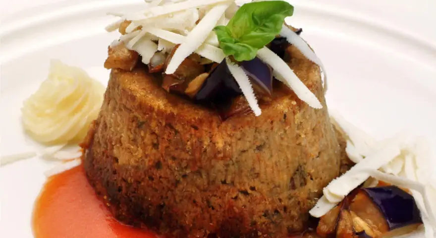 Sformato di melanzane leggero, guarnito con scaglie di formaggio, basilico e servito con salsa rossa e purè.