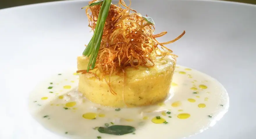 Flan di porri con salsa di acciughe, guarnito con cipolla croccante e erbe aromatiche. Un piatto raffinato che celebra i sapori del mare e della terra.