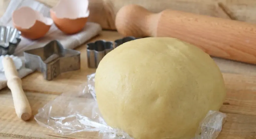 Impasto per kruche ciasto, stampini per biscotti, gusci d'uovo e mattarello pronti per preparare dolci deliziosi.