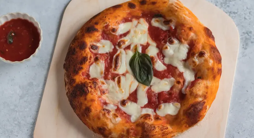 Pizza napoletana appena sfornata, con pomodoro, mozzarella filante e basilico fresco, pronta per essere gustata.