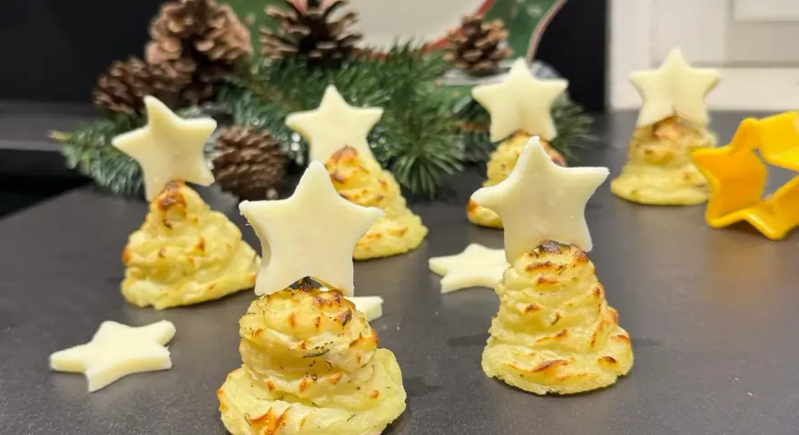 Alberelli di patate decorati con stelle di formaggio, su un piatto natalizio con pigne e rami di abete.