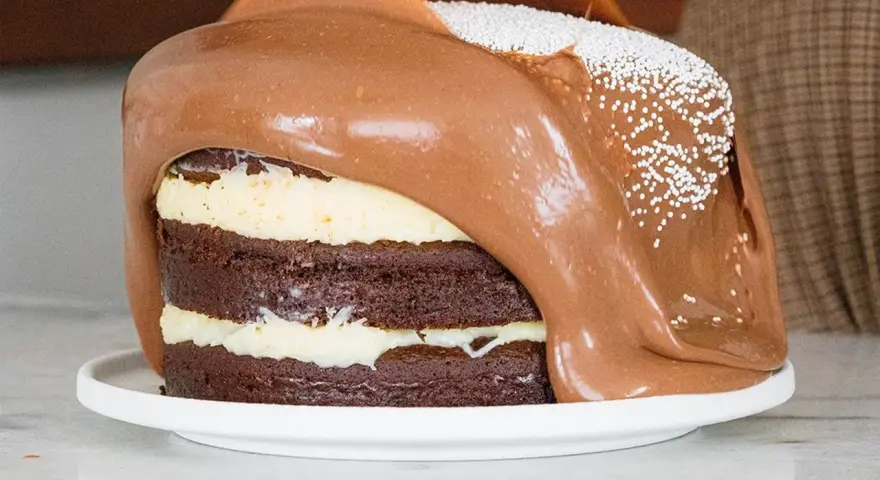Torta al cioccolato a strati con glassa al cioccolato fusa che cola, decorata con perline bianche. Un vero tsunami di dolcezza!