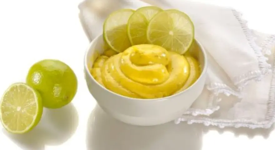 Una ciotola di cremosa crema al lime, guarnita con fette di lime fresco e accompagnata da lime interi e a metà.